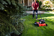 Photo of CRAFTSMAN lawn mower CM11A-02T8793 on grass, being pushed outdoors near pine tree.