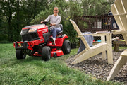 Photo of Craftsman riding lawn mower CM13APA9ZSA93 in use on green grass near outdoor chairs.