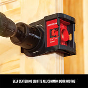 Craftsman self-centering door lock jig CMAH1MDL shown attached to wooden door with drill inserted.