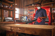 Photo of Craftsman handheld blower CMCBL0100B in use cleaning a wooden workbench in a workshop.