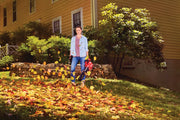 Photo of person using Craftsman leaf blower CMCBL700B outdoors, blowing autumn leaves on grass near yellow house.