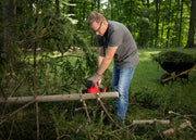 Photo of Craftsman CMCCS320D1 chainsaw cutting a tree branch outdoors, wheelbarrow visible in background.