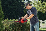 Photo of person trimming hedge with red Craftsman hedge trimmer, SKU CMCHT810B, in outdoor garden setting.