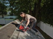 A person wearing safety gear is working on a rooftop using a red CRAFTSMAN branded cordless nailer. The person appears to be