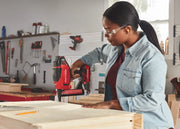 Photo of person using Craftsman cordless nailer CMCN618NB on wood in a workshop, wearing a denim shirt.