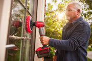 Photo of Craftsman CMCPSMFB cordless power scrubber cleaning a window, red and black design, in outdoor use.