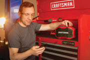 Photo of a person using a Craftsman CMCR001B jobsite Bluetooth speaker on a red tool chest, with other Craftsman tools nearby.