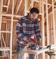 Photo of a Craftsman CMCS550B circular saw cutting a wooden board at a construction site, person in plaid shirt operating tool.