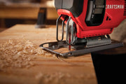 Photo of Craftsman jigsaw CMCS600D1 cutting wood, close-up of blade and base with wood shavings around.