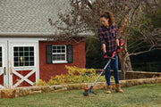 Photo of a person using a CRAFTSMAN string trimmer outdoors, SKU CMCST920B, trimming grass near a house and yard.