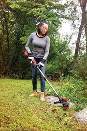 Person using CRAFTSMAN CMCST920M1 string trimmer in a garden, trimming grass near rocks and plants.
