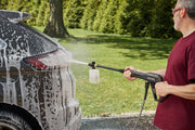 Photo of person using CRAFTSMAN CMEPW1800 pressure washer with soap dispenser to clean soapy car outdoors.