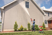 Person using Craftsman CMEPW2400 pressure washer to clean exterior house siding, red unit visible on lawn.