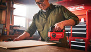 Photo of Craftsman jigsaw CMES610 cutting wood in workshop, red tool cabinets visible in background.
