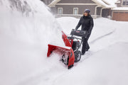 Photo of a person using a Craftsman snow blower outdoors in heavy snow, SKU CMGB223101, clearing a driveway.