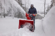 Photo of a person using a red Craftsman snow blower, SKU CMGB223104, clearing snow on a driveway in winter.
