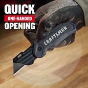Photo of Craftsman folding utility knife CMHT10350 held in a gloved hand, showing black blade and quick-open feature.