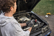 Person wearing gloves holds a set of hex keys while working on the engine bay of a car with the hood open. A soccer ball and