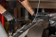 A close-up of a person wearing black gloves using a CRAFTSMAN T-handle hex key to work on a car engine component.