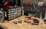 A set of CRAFTSMAN screwdrivers with red and black handles arranged on a wooden workbench in a workshop. Behind the