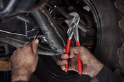 Photo of a person using Craftsman pliers with red handles, SKU CMHT82250, on vehicle suspension components.