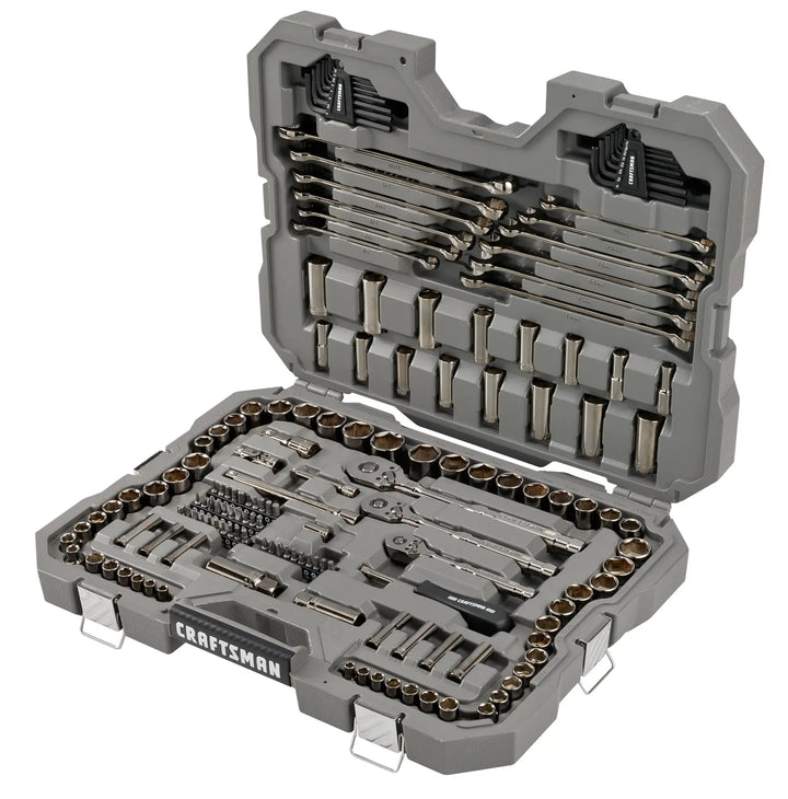 A grey, hard plastic Craftsman tool case is open, showing a comprehensive socket and wrench set. The organized interior contains various sizes of wrenches, sockets, ratchets, screwdriver bits, hex keys, and extensions, all neatly arranged in secure slots.