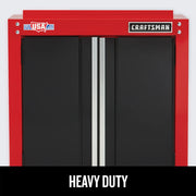 Front view of a heavy duty wall cabinet with two black doors, red frame, and silver vertical handles. The cabinet has a 'CRAFTSMAN' logo on the top right and a 'Made in USA with global materials' sticker on the top left. The text 'HEAVY DUTY' is displayed at the bottom.