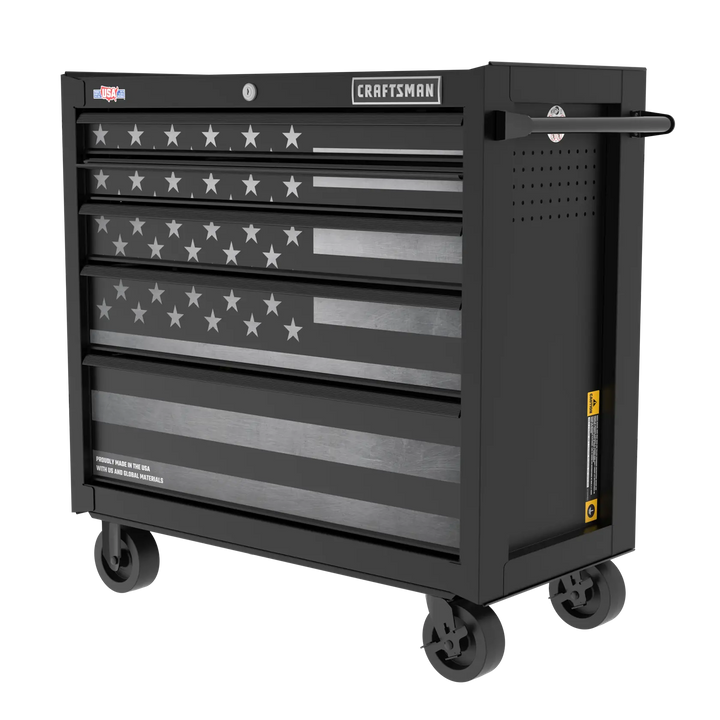 A black rolling tool chest with multiple drawers, featuring an American flag design on the front. The chest has caster wheels for mobility and a handle on the side. The brand name 'Craftsman' is displayed at the top.