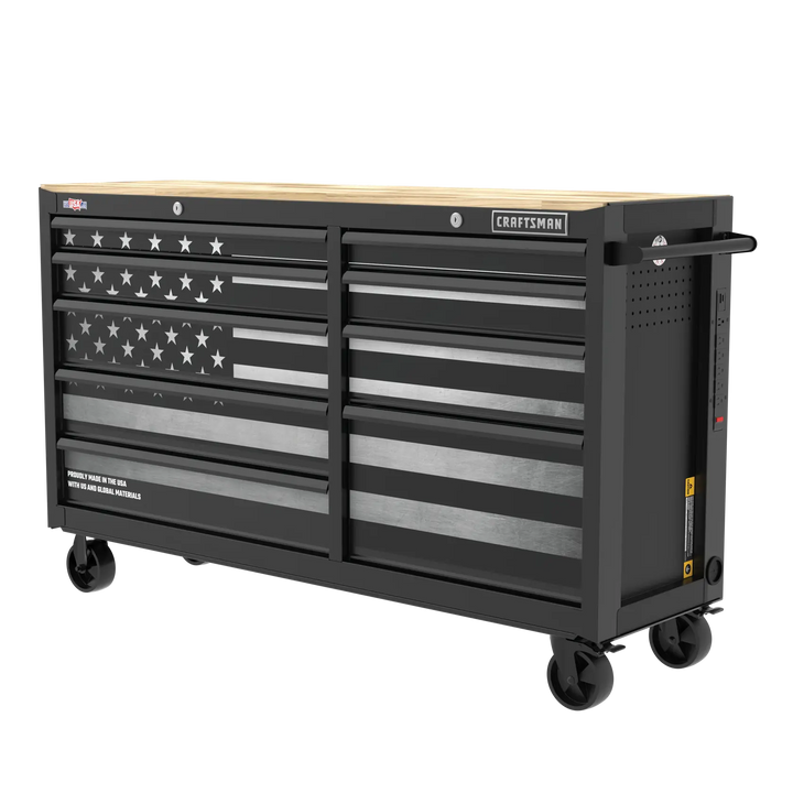 Large black rolling tool chest with multiple drawers, featuring an American flag design on the front and a light wood top. The chest is labeled with the brand name 'Craftsman' and has casters for mobility.