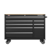 A black rolling tool chest with multiple drawers and a wooden top, featuring metal handles and caster wheels for mobility. The chest is branded with a Craftsman logo on the upper right corner.