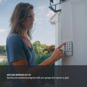 Photo of person pressing CRAFTSMAN garage keypad, SKU CMX348, outdoor setting, product installed on white wall.