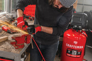 Photo of person using a Craftsman air compressor CMXECXM331 in a workshop, grinding metal with visible sparks.