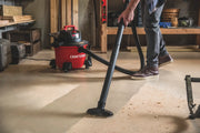 Person using a CRAFTSMAN wet/dry vacuum, SKU CMXEVBE17584, cleaning sawdust on a workshop floor.