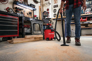 Photo of CRAFTSMAN CMXEVBE17590 wet/dry vacuum cleaning sawdust on a workshop floor, person holding vacuum hose.