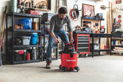 Photo of a person using a Craftsman wet/dry vacuum, SKU CMXEVBE17590, red and black, in a garage workshop.