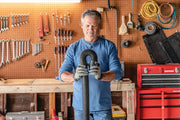 Photo of a person wearing gloves holding a Craftsman vacuum hose, SKU CMXEVBE17595, in a workshop setting.