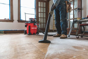 Photo of a worker using a Craftsman CMXEVBE17656 wet/dry vacuum to clean dust on a wooden floor during renovation.