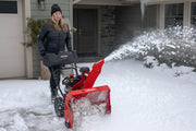 Photo of Craftsman snow blower SKU CMXGBAM213101 clearing snow in front of a house, operated by a person.