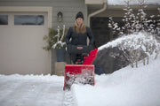Photo of person using Craftsman snow blower CMXGBAM213101 on driveway in winter, snow being expelled to the side.