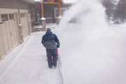 Photo of a person using a Craftsman snow blower SKU CMXGBAM213101 to clear snow from a driveway during winter.