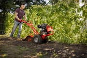 Photo of a person operating a CRAFTSMAN rear-tine tiller CMXGVAM1144037, tilling soil in a garden area.