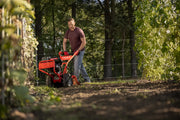 Photo of a person using a red Craftsman tiller, SKU CMXGVAM1144037, in a garden with green plants.