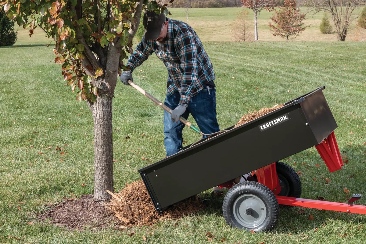 Photo of a Craftsman dump cart SKU CMXGZBF7124355 being used to unload mulch around a tree in a yard.