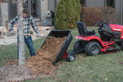 Photo of Craftsman dump cart SKU CMXGZBF7124489 attached to red Craftsman lawn tractor, unloading mulch next to a tree.