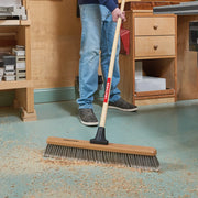 Photo of a person using a CRAFTSMAN push broom, SKU CMXMLBA8224A, with wood handle and wide bristle head in a workshop.