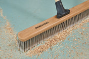 Photo of CRAFTSMAN push broom with wood handle SKU CMXMLBA8224A, sweeping sawdust on a blue floor, top view.