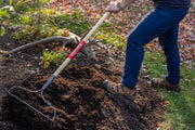 Photo of a person using a CRAFTSMAN garden rake, SKU CMXMLTP35315, on soil in a garden with autumn leaves.