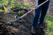 Photo of a person using a CRAFTSMAN garden fork SKU CMXMLTP35325 with wood handle and black metal tines in a garden.