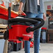 Photo of CRAFTSMAN portable wet/dry vacuum CMXZVBE43271 with black hose and wheels being carried in workshop.