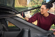 A person wearing black gloves and a maroon shirt uses a CRAFTSMAN tool to work on the rear interior area of a car with the